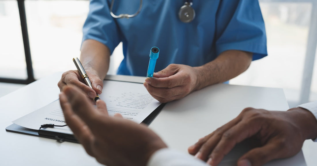 A doctor talking with a patient at their desk. The doctor writes in a clipboard while holding a blue test tube.