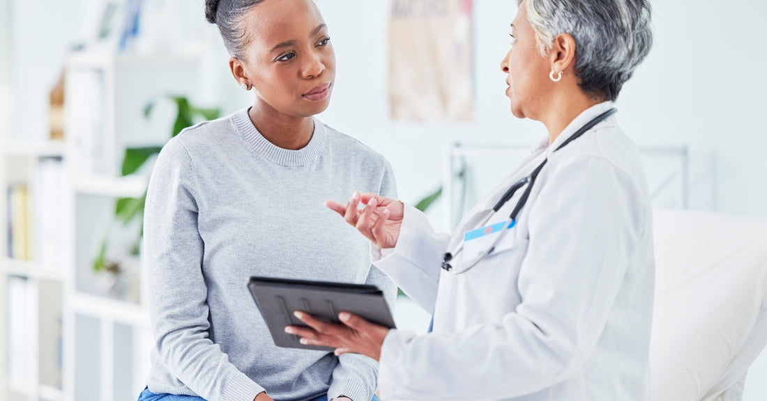 A doctor talking to a patient in their office. The doctor holds a small black tablet in their left hand.