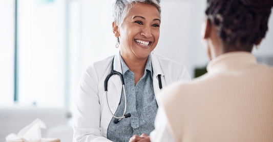 Doctor with a stethoscope around their neck at their desk smiling at a patient sitting across from them.